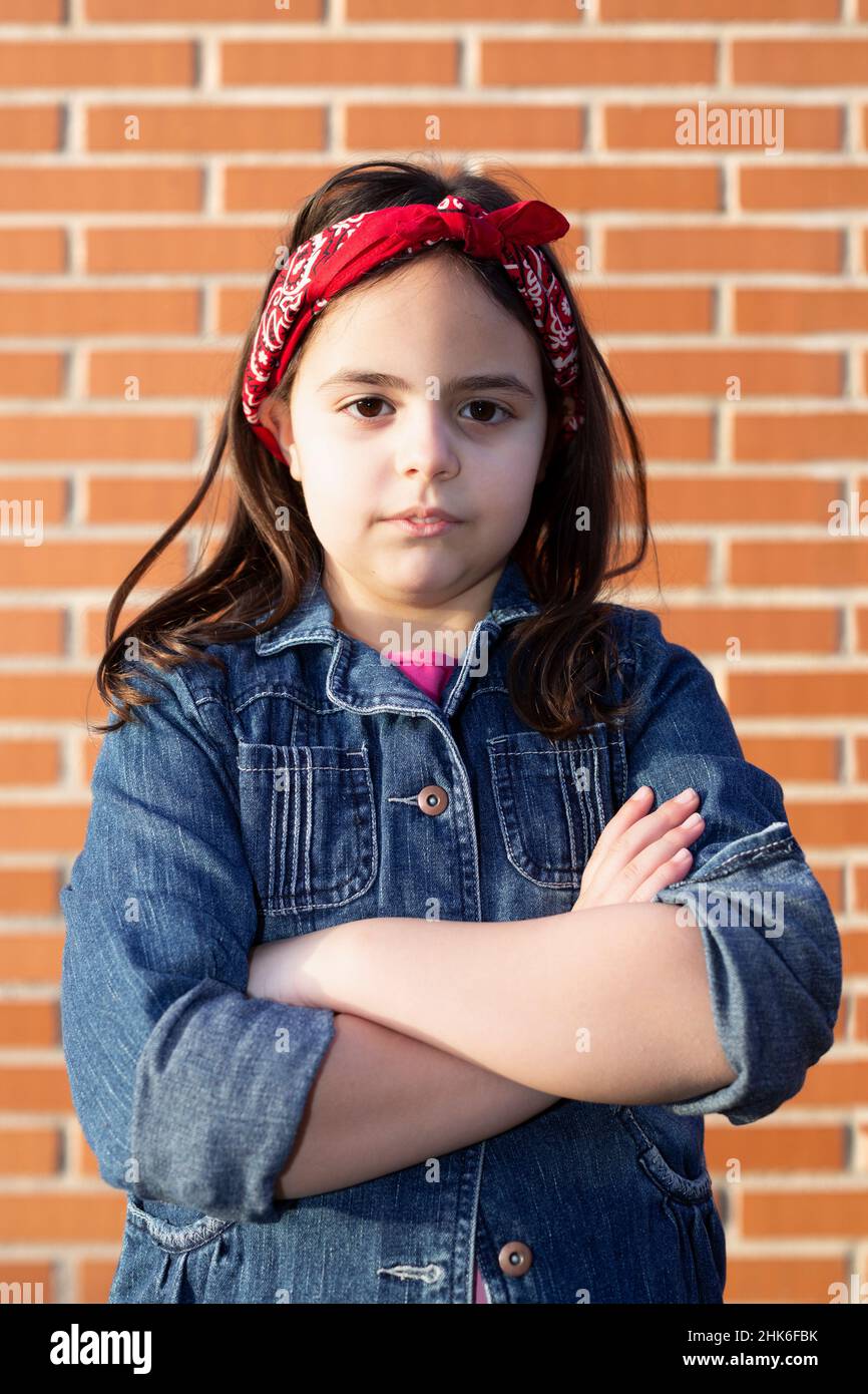 Portrait of little caucasian girl with crossed arms in serious attitude. She is isolated on a brick wall. Feminism and girl power concept. Stock Photo