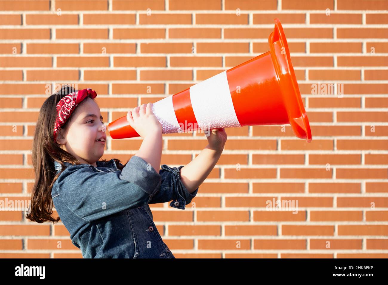 Child activist isolated on brick wall shouting through megaphone. Concept of equality and defense of women's rights. Stock Photo