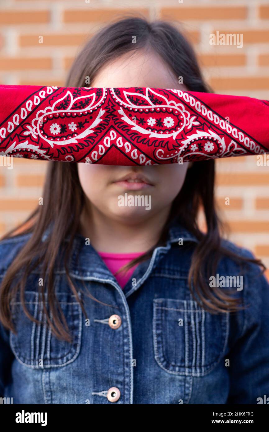 Close up of the face of a little girl with her eyes covered by a handkerchief. Face without identity, unrecognizable person. Stock Photo