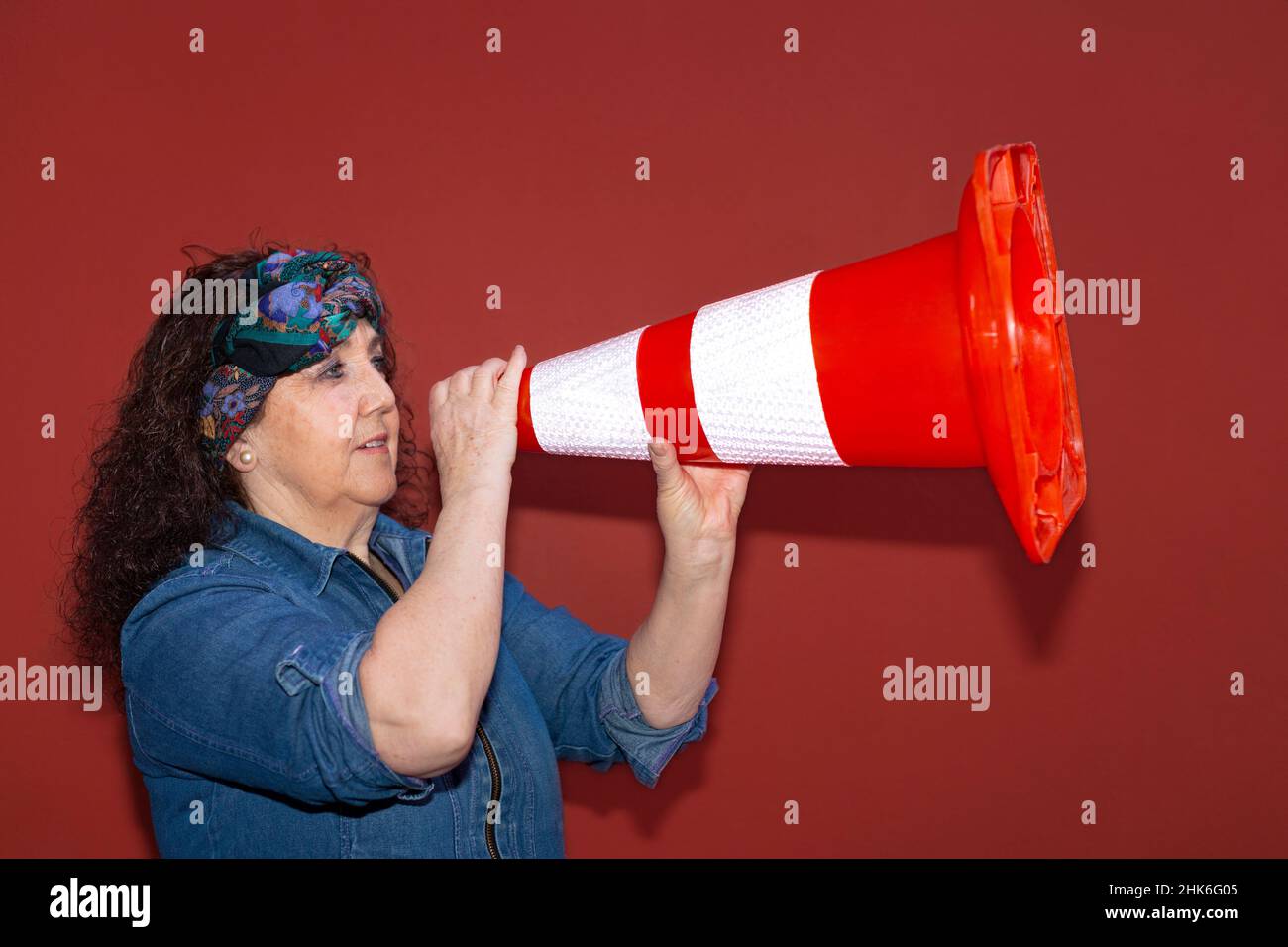 Older woman in protest clothing holding a megaphone. She is isolated on red background. Concept of feminism, fighting woman and Women's Day. Stock Photo