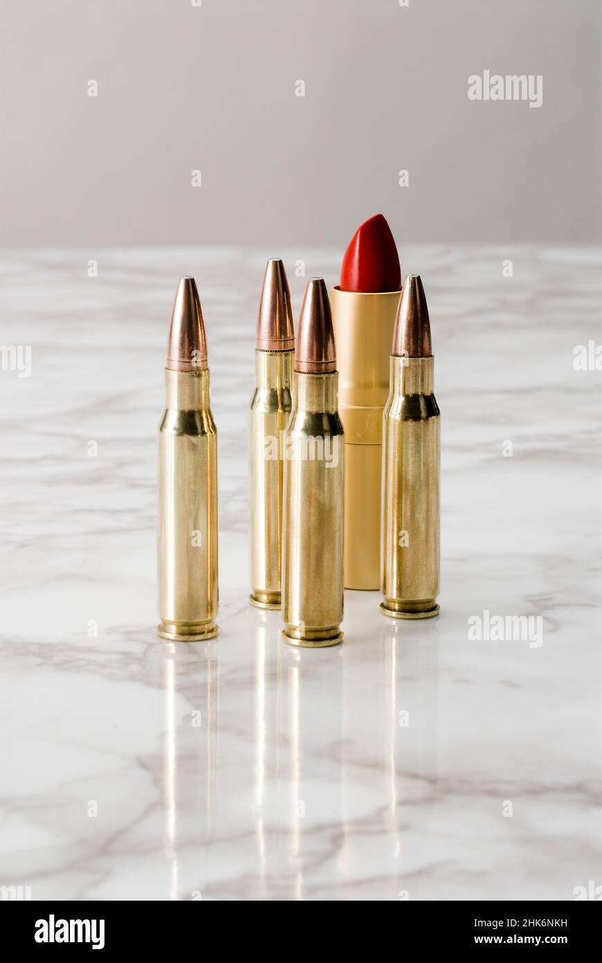 Group of bullets and a red lipstick standing up on a marble surface ...