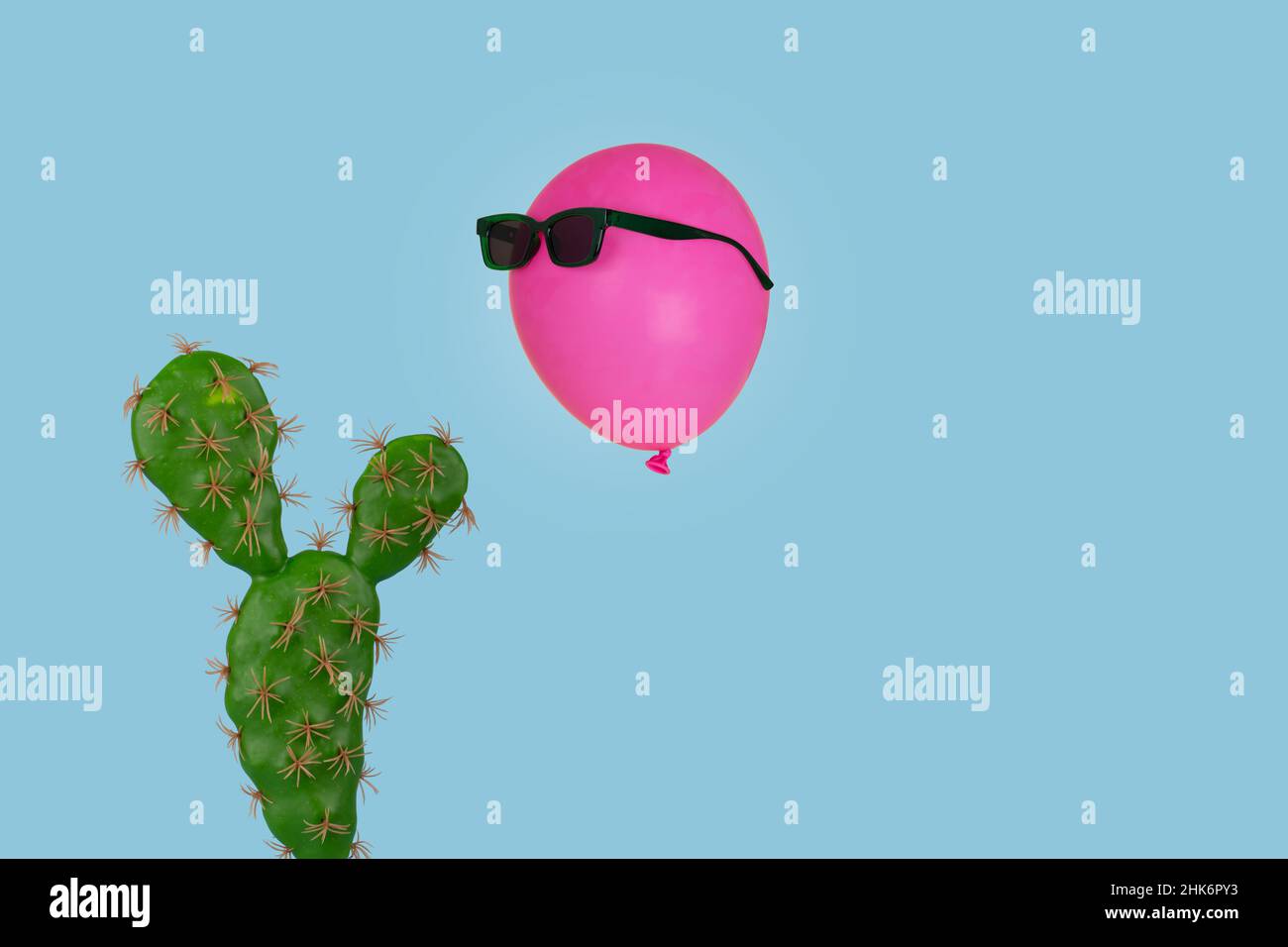 Cactus plant with above it floating a pink balloon in sunglasses isolated on a bright blue background. Creative minimal concept.  Use for card, poster Stock Photo