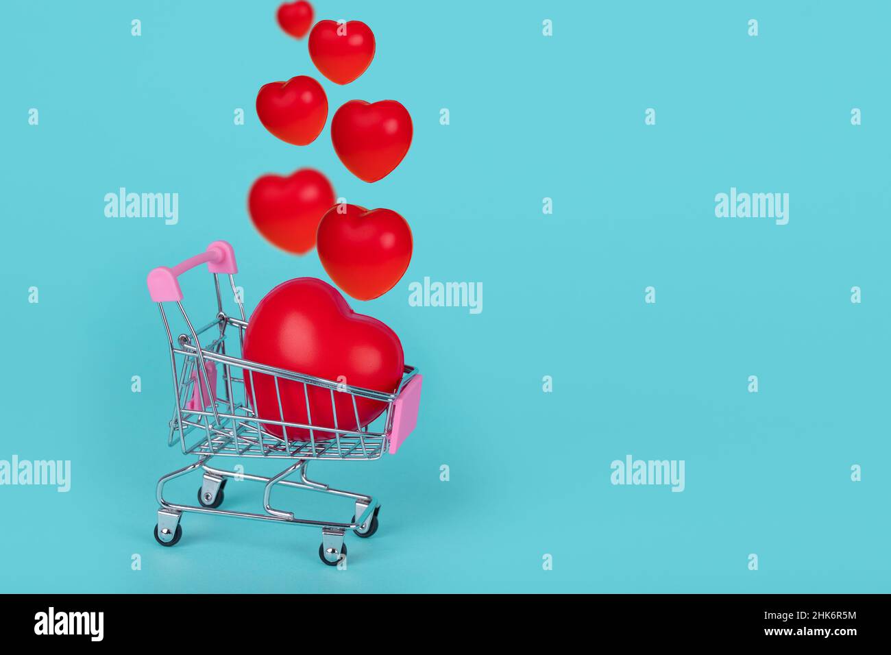 Shopping trolley with red hearts on turquoise background. Creative idea for Valentines, Mothers or International Women's Day shopping and sale. Copy s Stock Photo