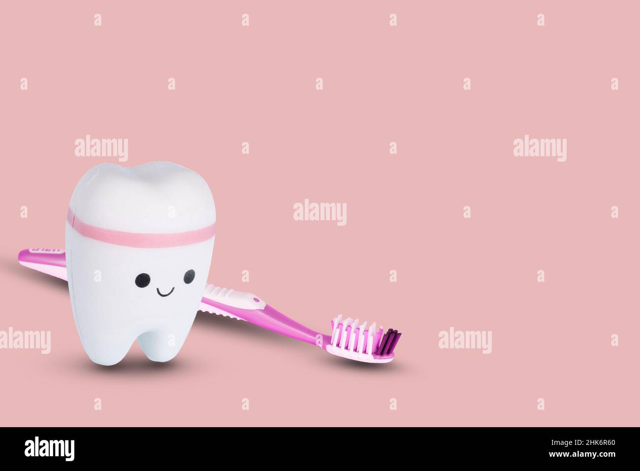 Toothbrush and white tooth on a light pink background. Creative concept of dental examination teeth, dental health and hygiene. Copy space. Stock Photo