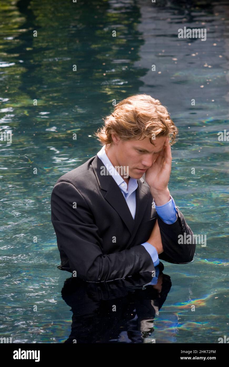 Young man wearing business suit, standing waist deep in water, hand on his face Stock Photo