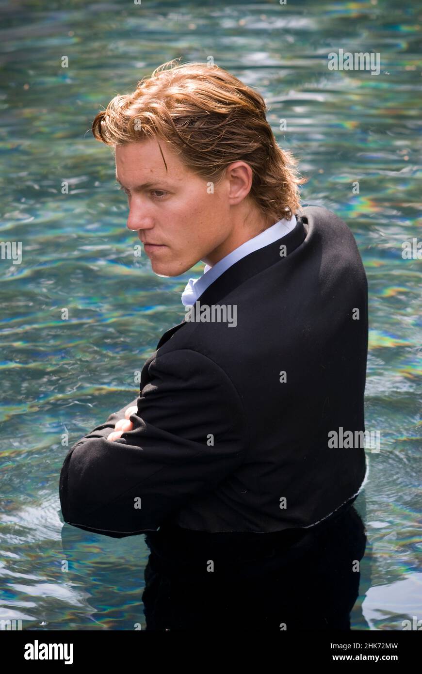 Young man wearing a business suit standing in water, arms folded in front of him Stock Photo
