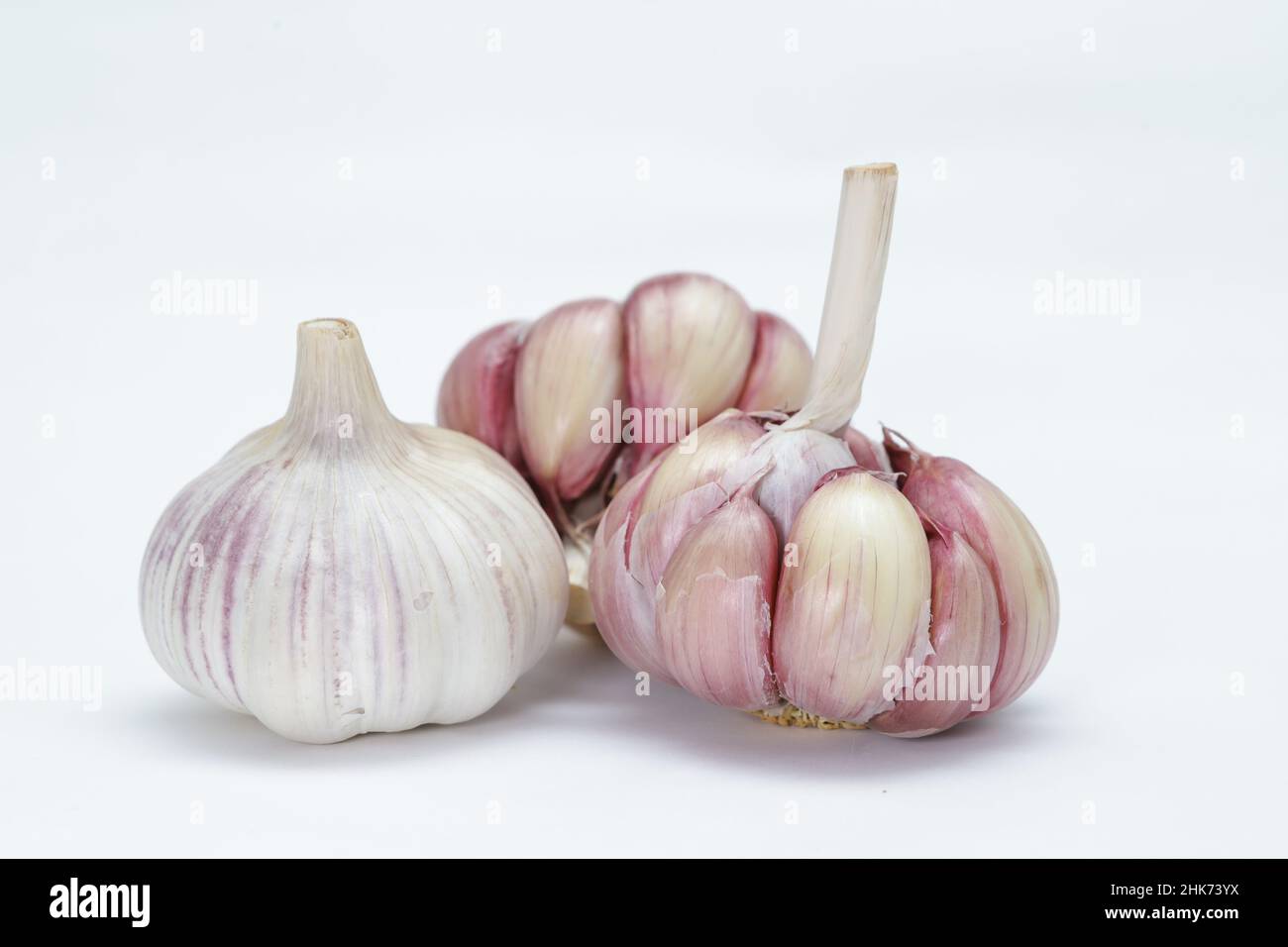 Three heads of garlic (Allium sativum), with one still unpeeled and the other two lightly peeled, each clove can be seen in rosy tones on the edges an Stock Photo