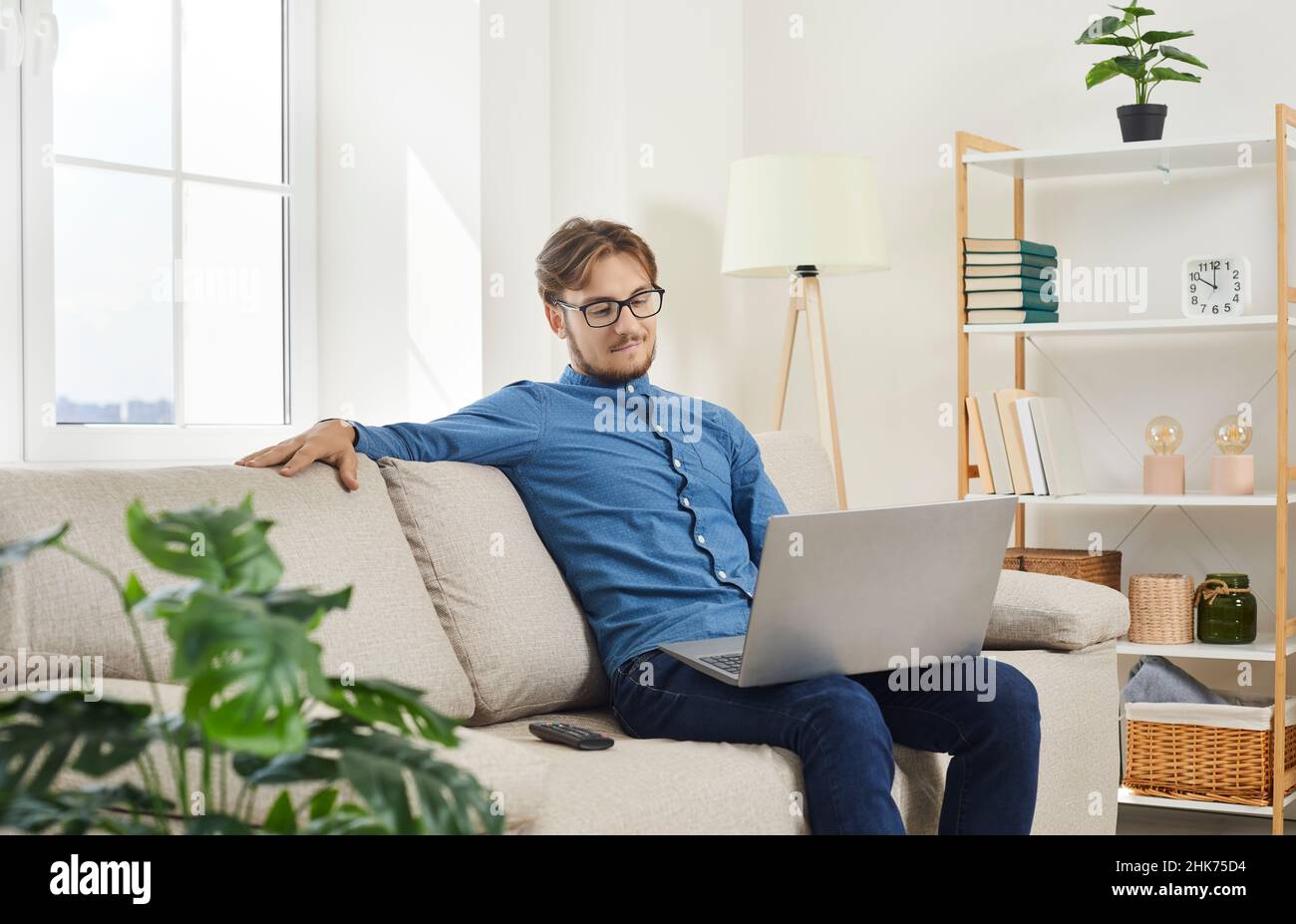 Young attractive man sitting on sofa at home working online on laptop or using internet. Stock Photo