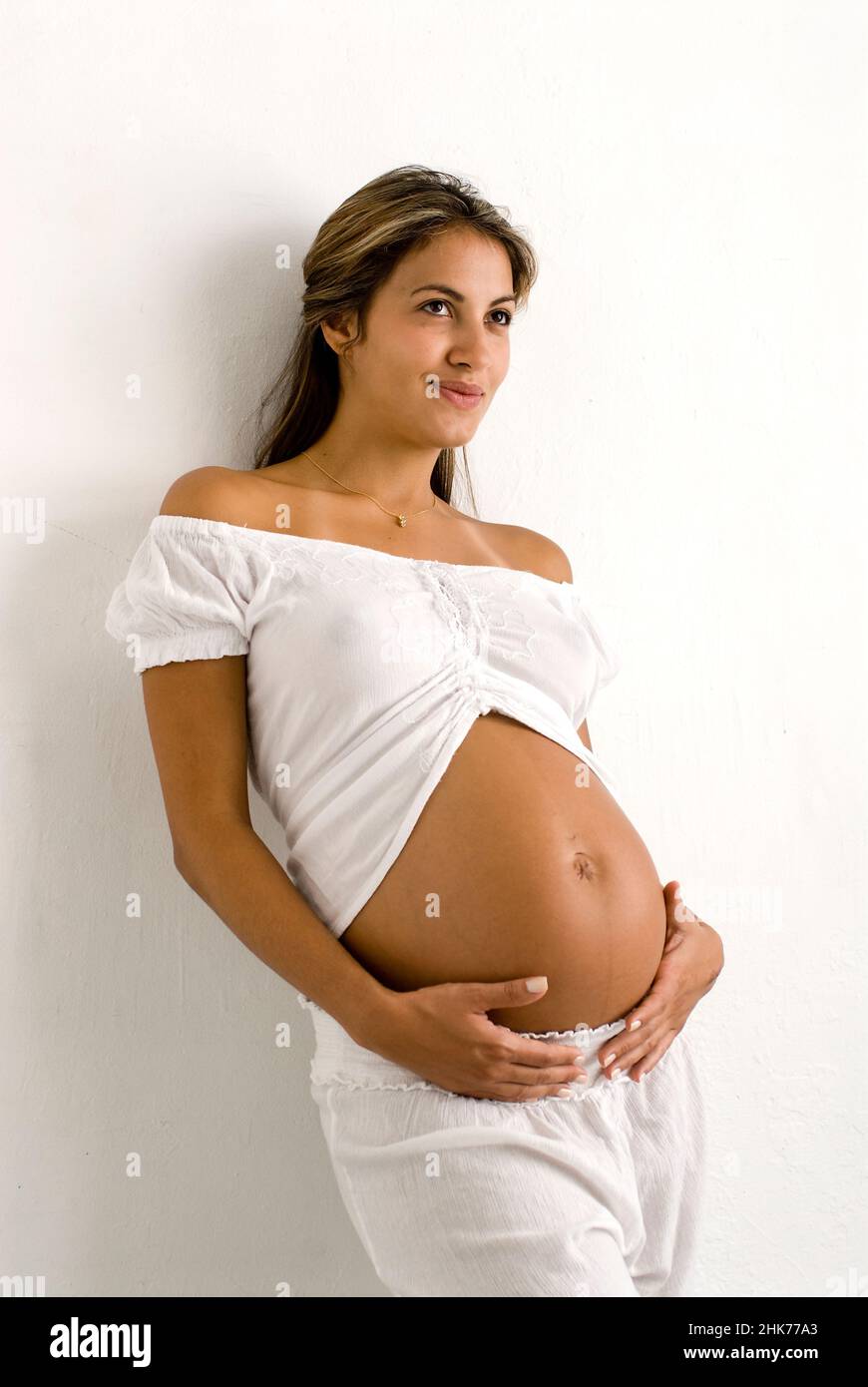 Portrait of young pregnant Hispanic woman, facing forward, holding belly Stock Photo