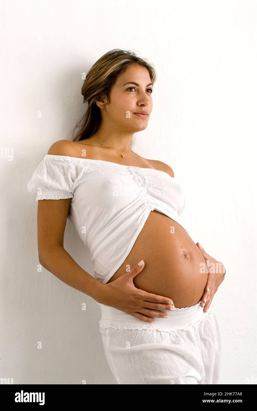 Portrait of young pregnant Hispanic woman, facing forward, holding belly Stock Photo