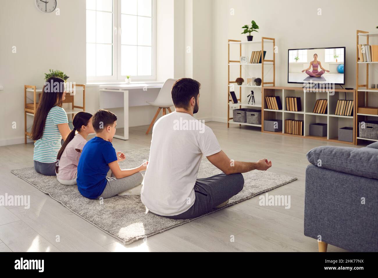 Family watching online yoga class on television and doing yoga exercises together Stock Photo