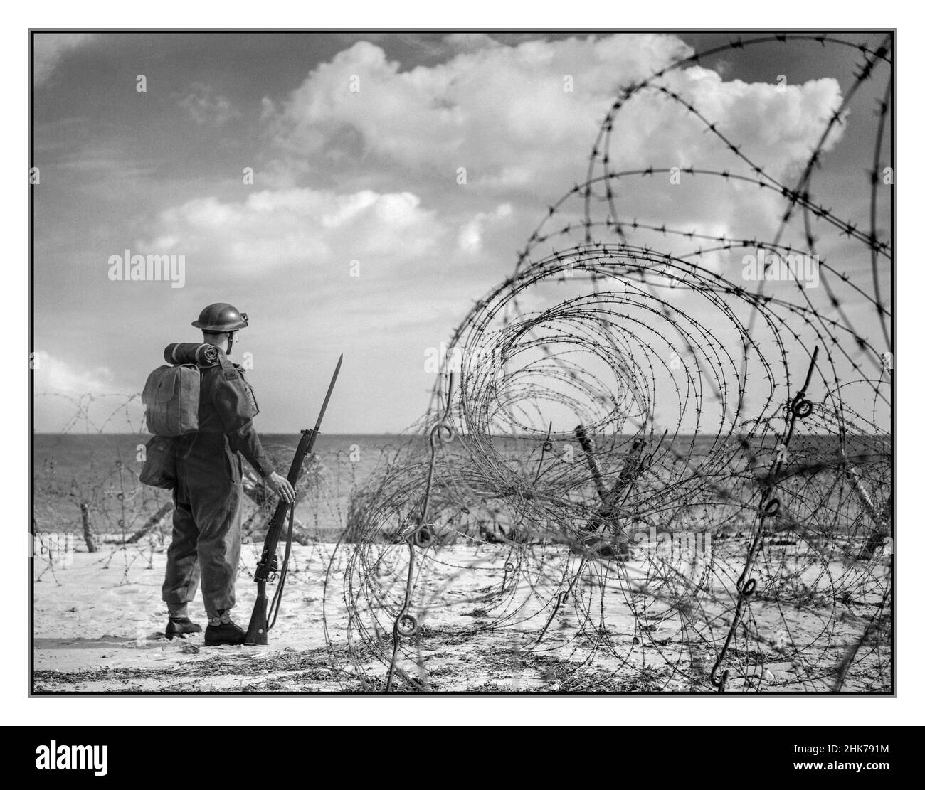 WW2 propaganda photograph of a British soldier in full wartime kit and uniform with rifle and fixed bayonet standing guard on a beach in southern England,  October 1940. World War II  British anti-invasion preparations of the Second World War entailed a large-scale division of military and civilian mobilisation in response to the threat of invasion (Operation Sea Lion) by German armed forces in 1940 and 1941. 1.5 million men were enrolled as part-time soldiers in the Home Guard. The rapid construction of field fortifications transformed much of the United Kingdom, especially southern England, Stock Photo