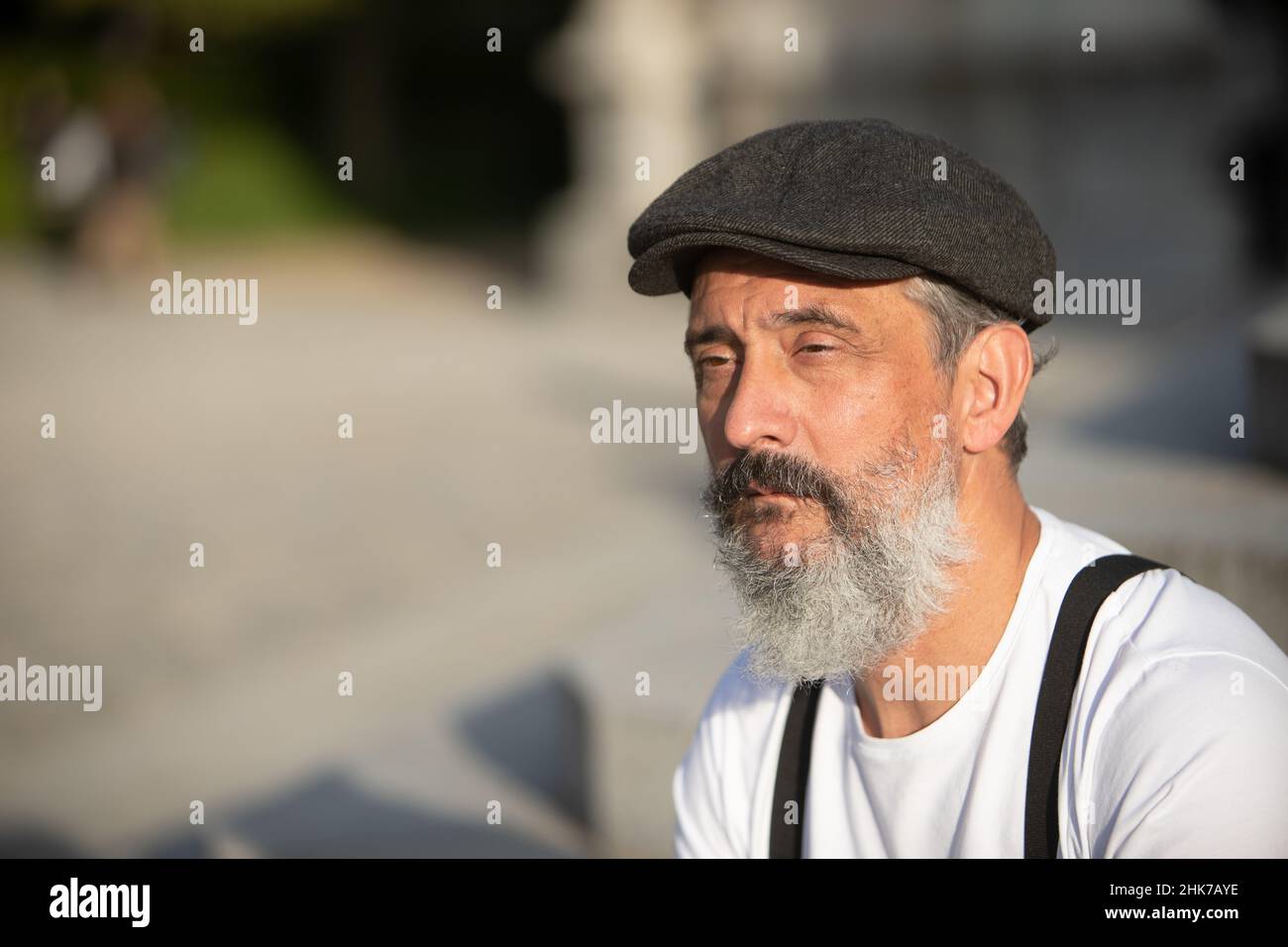 portrait of Older man with beret and gray beard sitting in a plaza Stock Photo