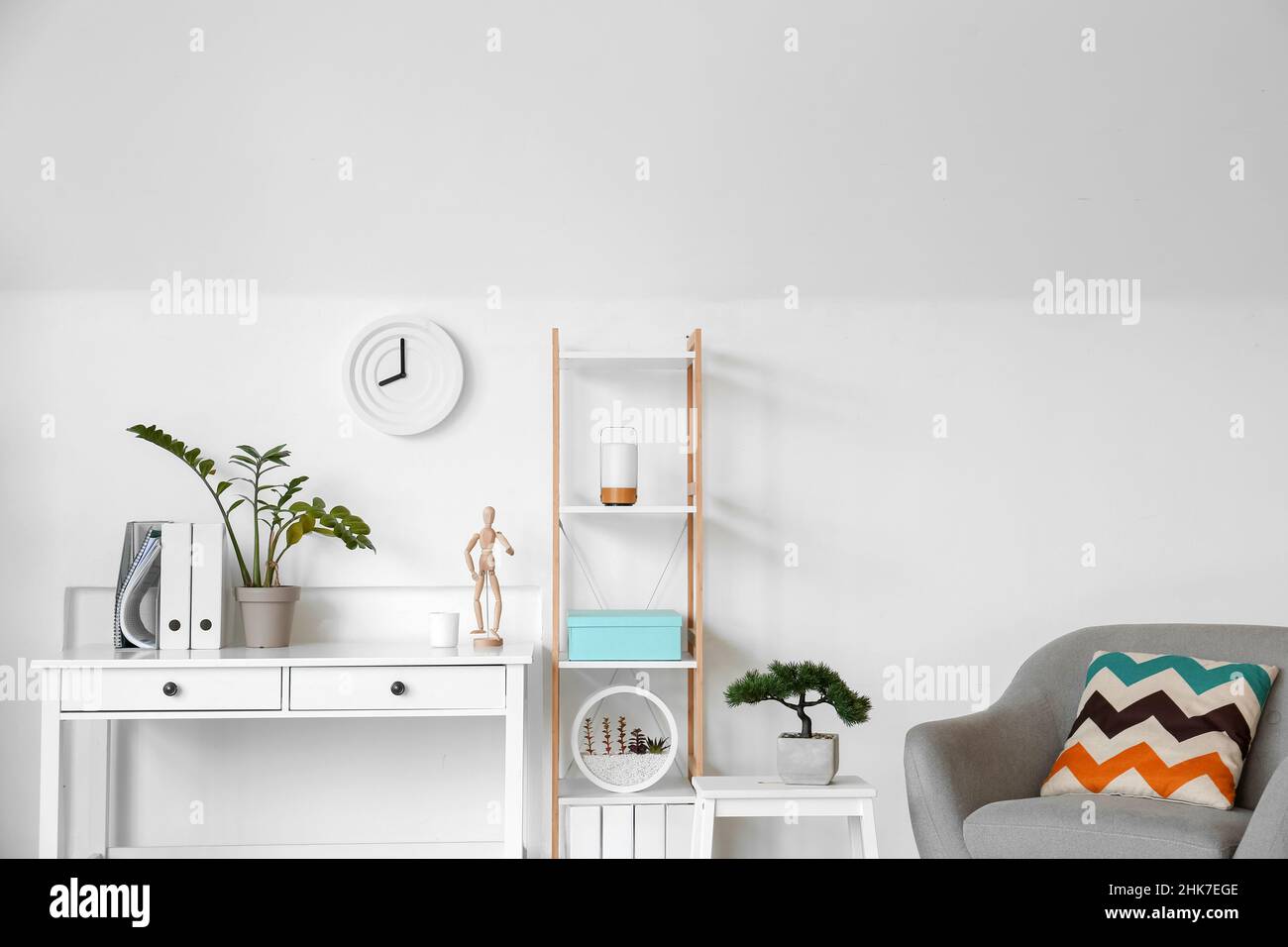 Interior of light living room with clock, table and shelving unit Stock