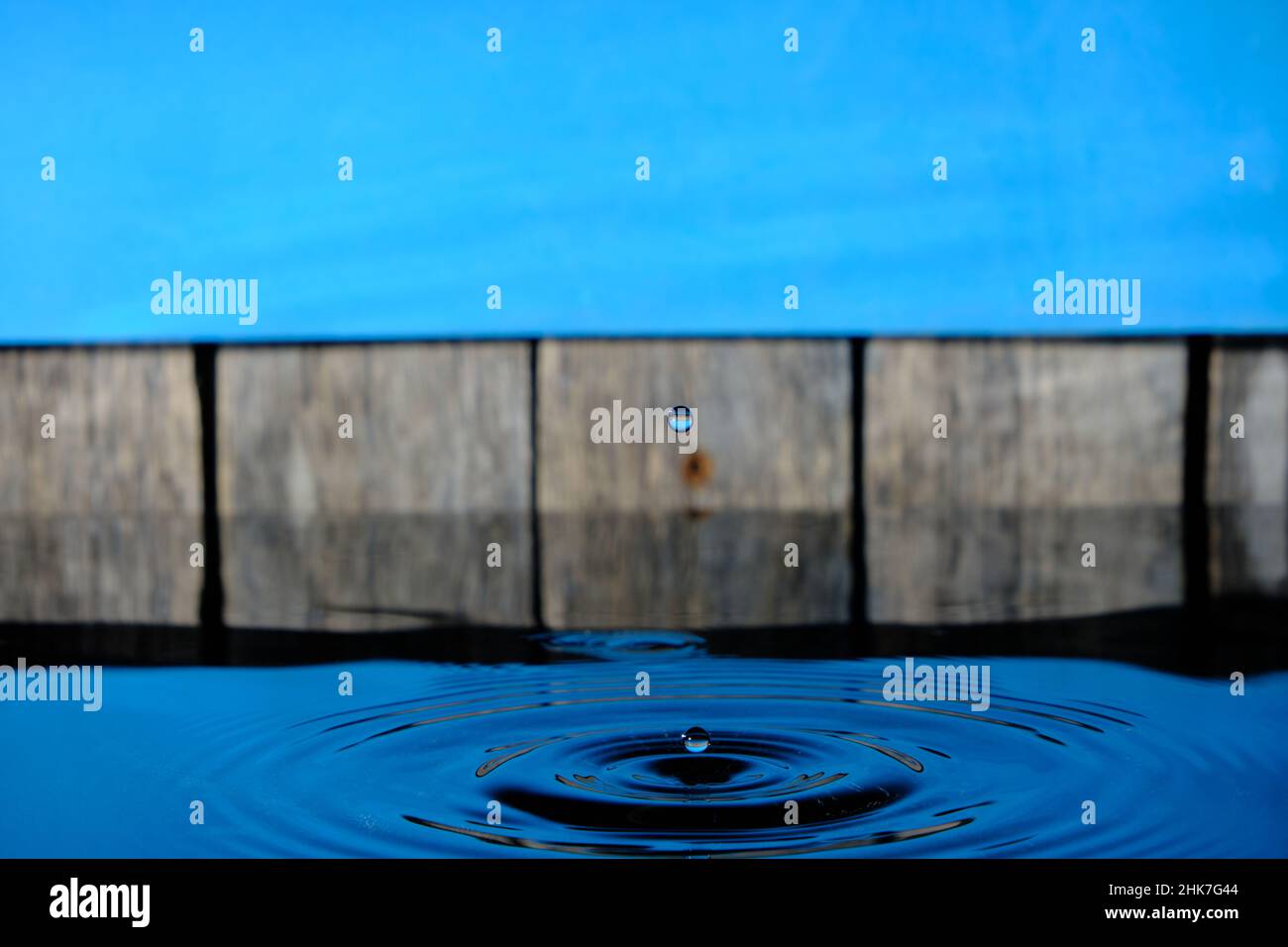 Circles and splash on water from raindrops on background an old fence and blue sky Stock Photo