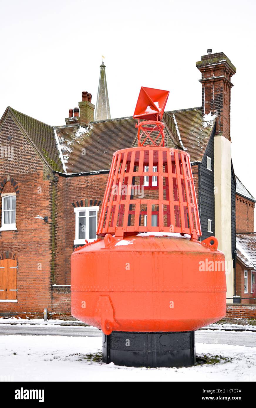 A large red buoy stands as a statue outside a historic house in the seaside town of Harwich, Essex, UK. The spire of St Nicholas Church is seen. Stock Photo
