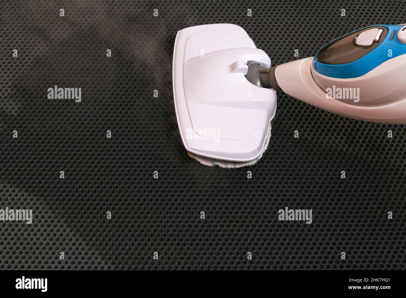 A man washes a black door mat with a steam mop. Killing germs, clean floor