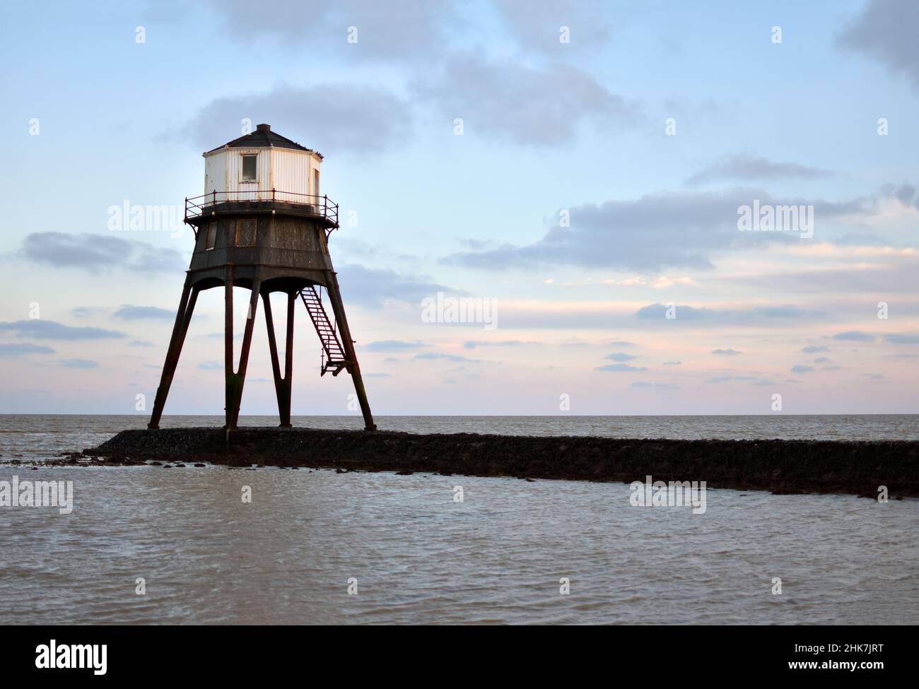 The historic stone causeway leads out towards the victorian Dovercourt Lighthouse in Dovercourt Bay seen as sunset colours enter the sky, Essex, UK Stock Photo