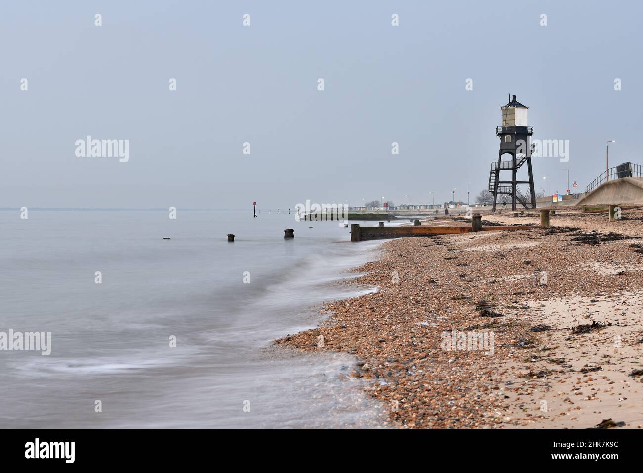 A long exposure shot of waves breaking on the stoney beach in front of the Dovercourt Lighthouse on a misty afternoon, Harwich & Dovercourt, Essex, UK Stock Photo