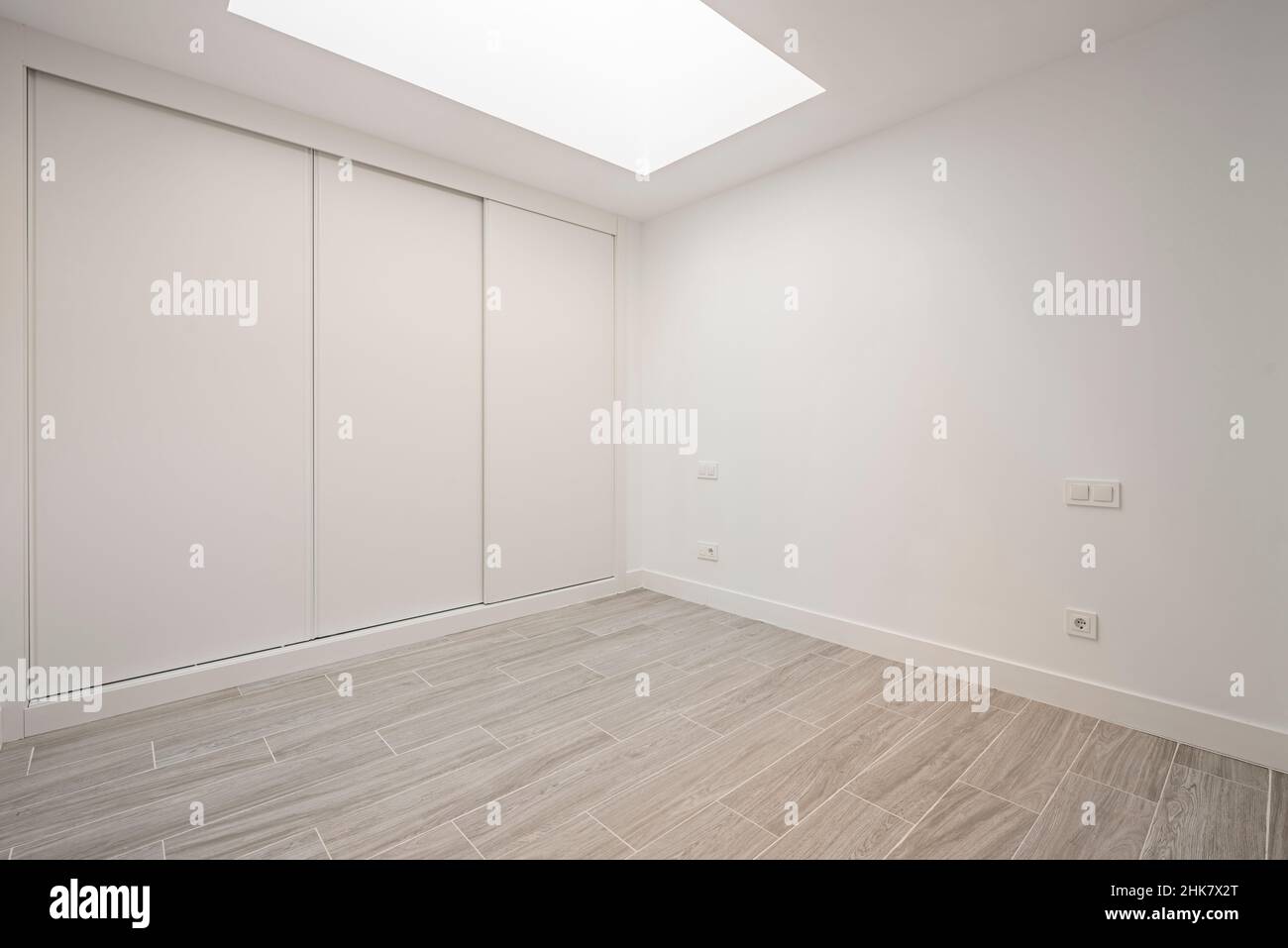 Angular view of a built-in wardrobe with white sliding doors and imitation wood stoneware floors and a skylight in the ceiling Stock Photo