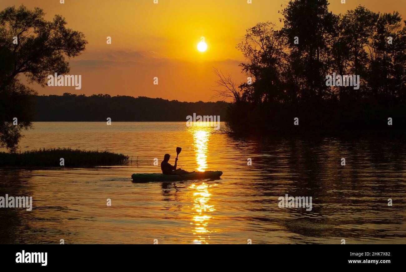 Woman paddles a kayak in the setting sun. Caesar Creek State Park, Waynesville, Ohio, USA. Stock Photo
