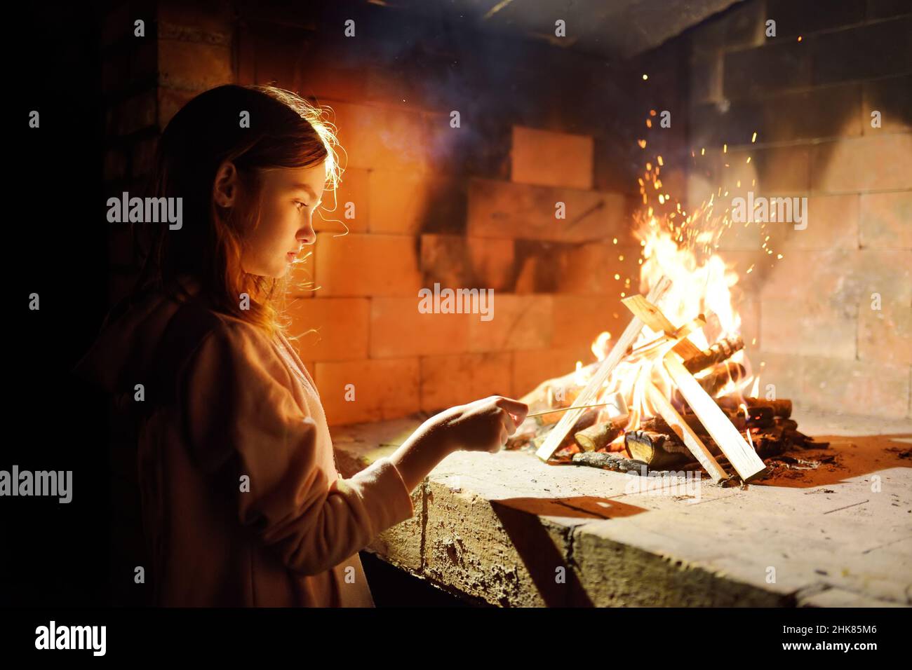 Adorable young girl roasting marshmallows on stick at bonfire. Child