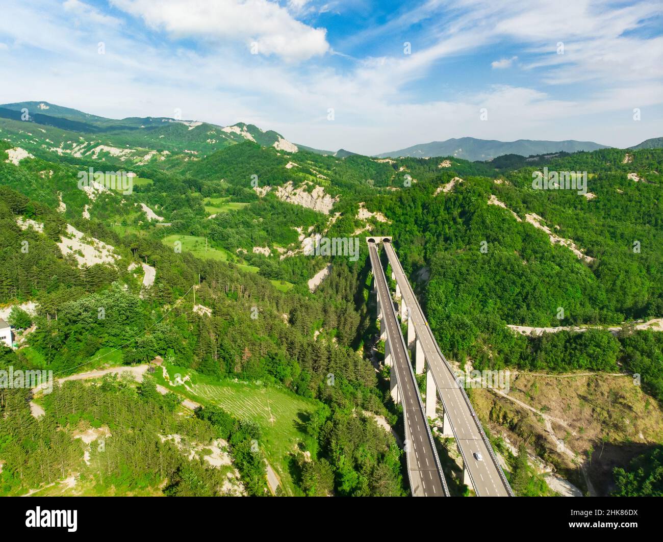 Aerial view of divided highway entering a mountain tunnel among green fields and hills surronding San-Marino microstate. Travelling across the beautif Stock Photo