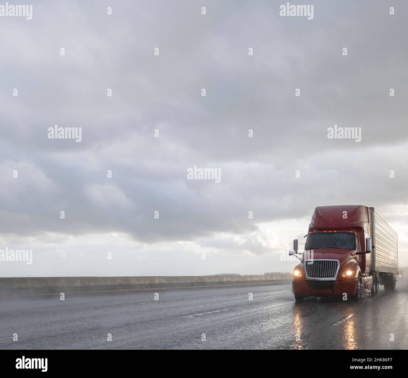 Bright red industrial big rig semi truck tractor for long haul transporting cargo on refrigerator semi trailer driving on the wide highway road with w Stock Photo