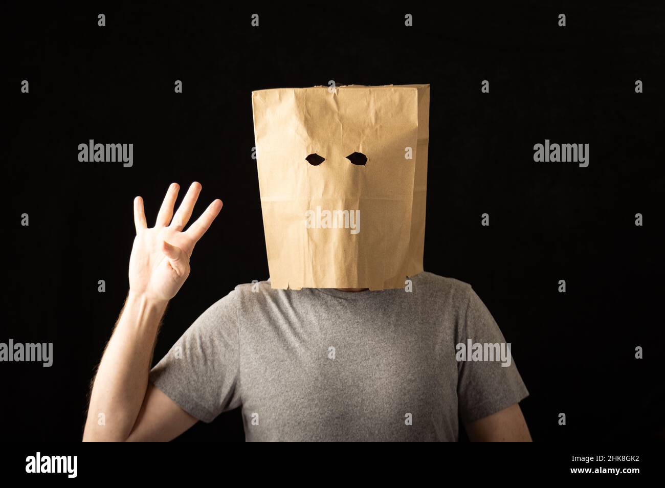 Man wearing a brown paper bag over his head and holding up four fingers