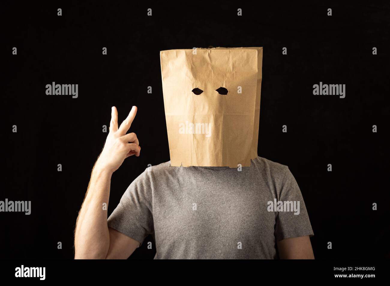 Man wearing a brown paper bag over his head and holding up two fingers