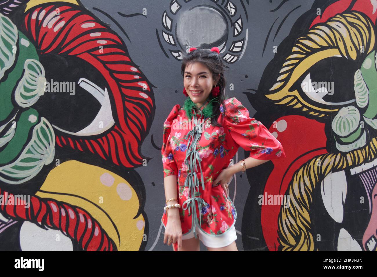 Young Thai Woman wears a traditional Chinese dress (cheongsam) and smiles for the camera  in front of a mural, Chinatown, Bangkok, Thailand Stock Photo