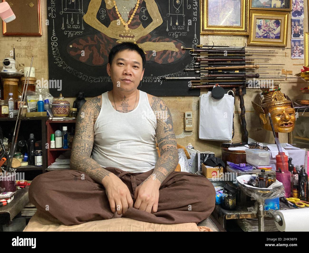 Bangkok, Thailand. 17th Jan, 2022. Sak Yant tattoo master Ajarn Neng sits in his store in Bangkok's On Nut district surrounded by tattoo sticks, ink, sculptures and images. His sacred tattoos are
