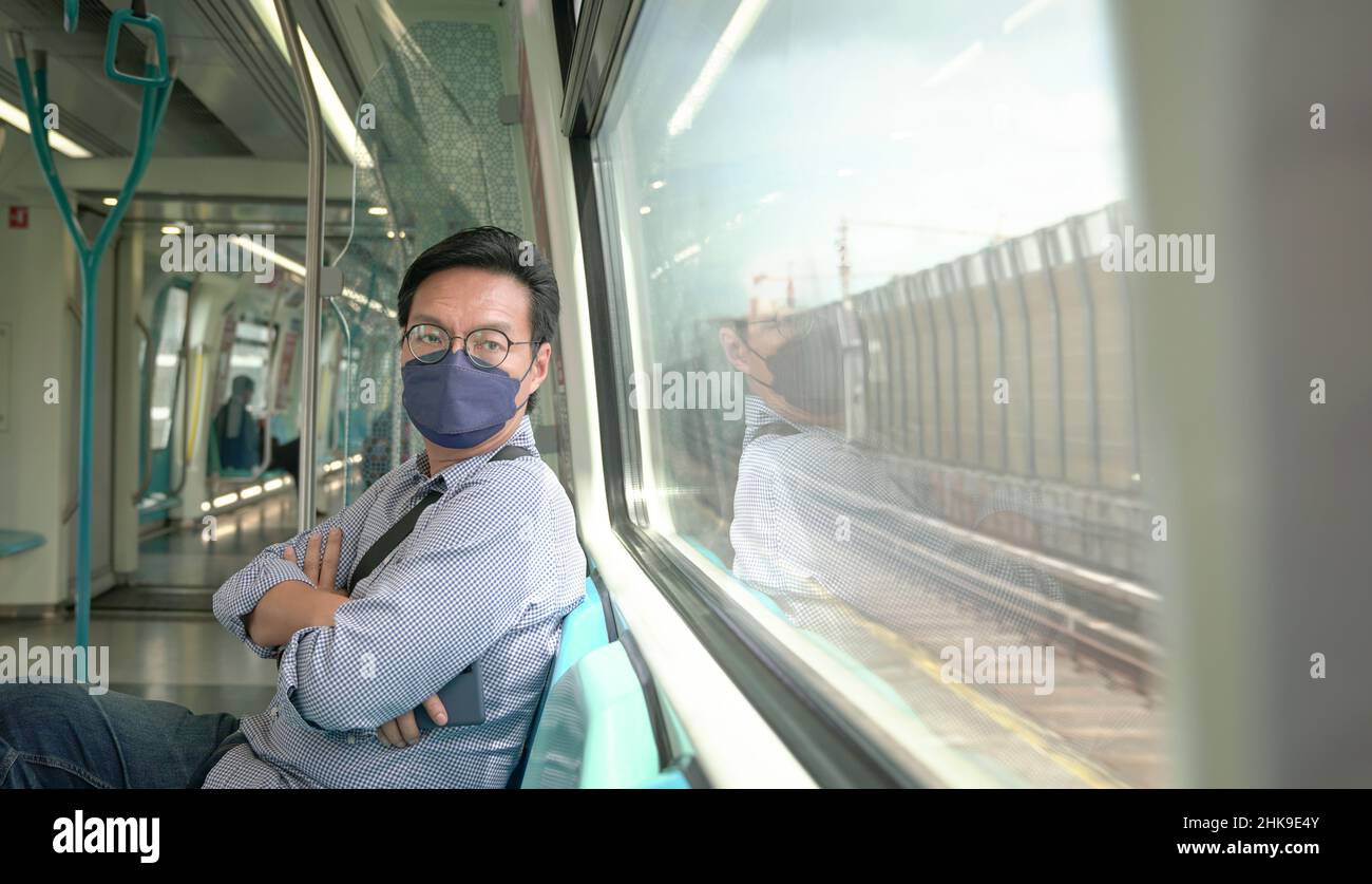 Asian man commuter with face mask on inside a moving subway train. Masked transit concept Stock