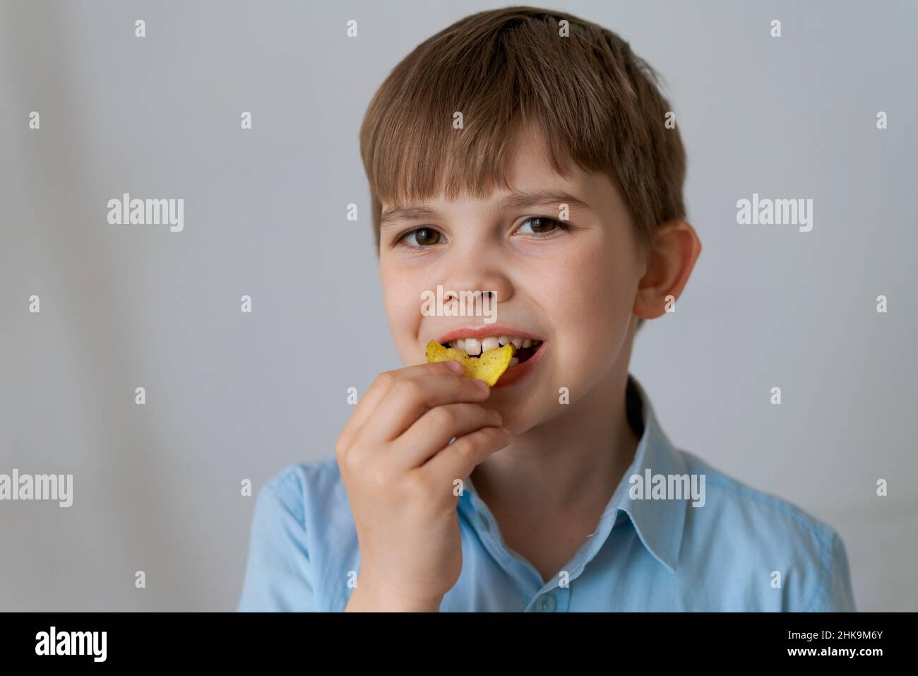 Close up portrait cheerful child having fun eating potato chips isolated on gray background. Cute little boy eating chips and smiling looking at the camera. Caucasian child eats junk food Stock Photo