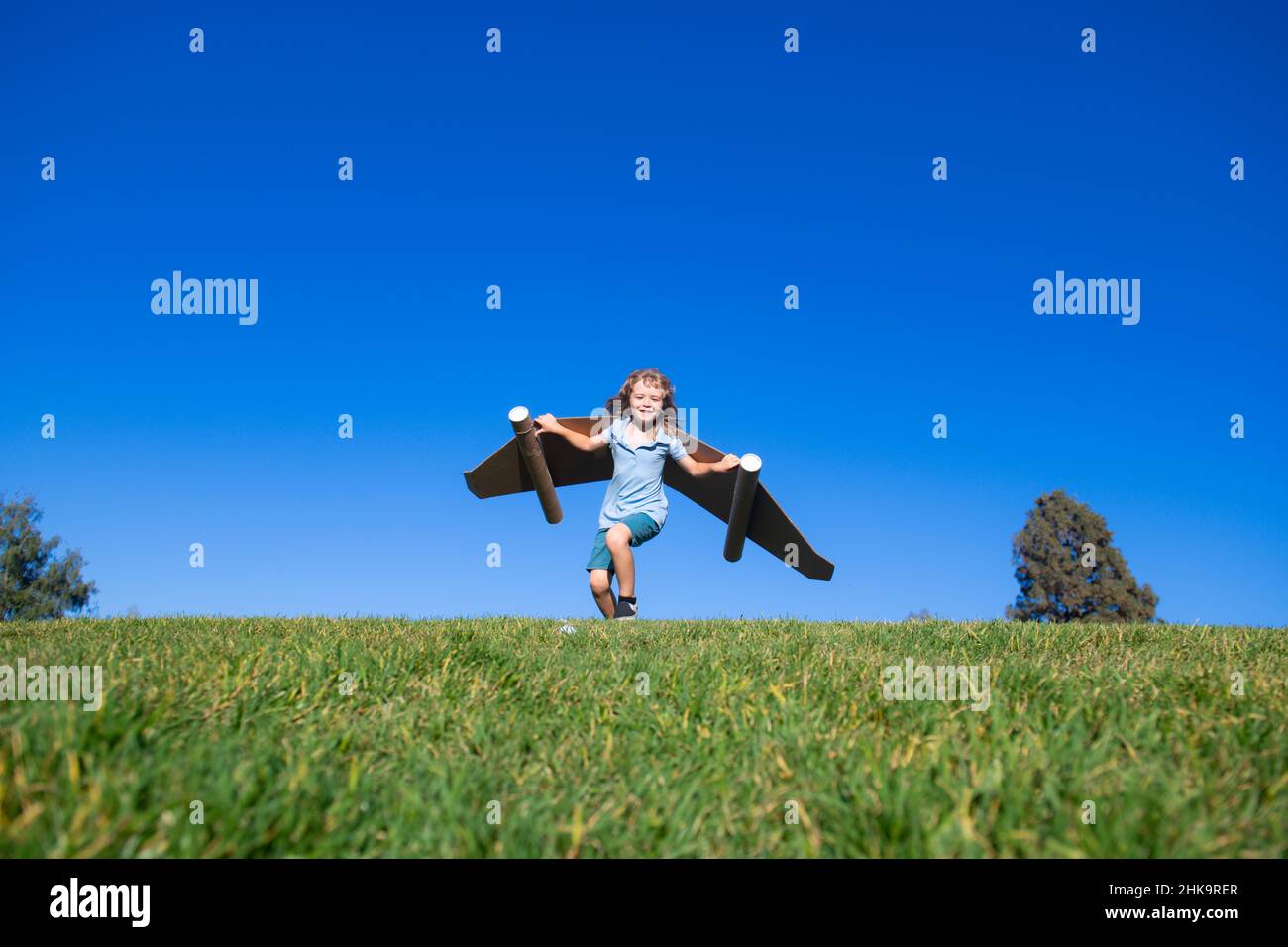 Happy child playing outside on green grass and blue sky. Kid pilot with ...