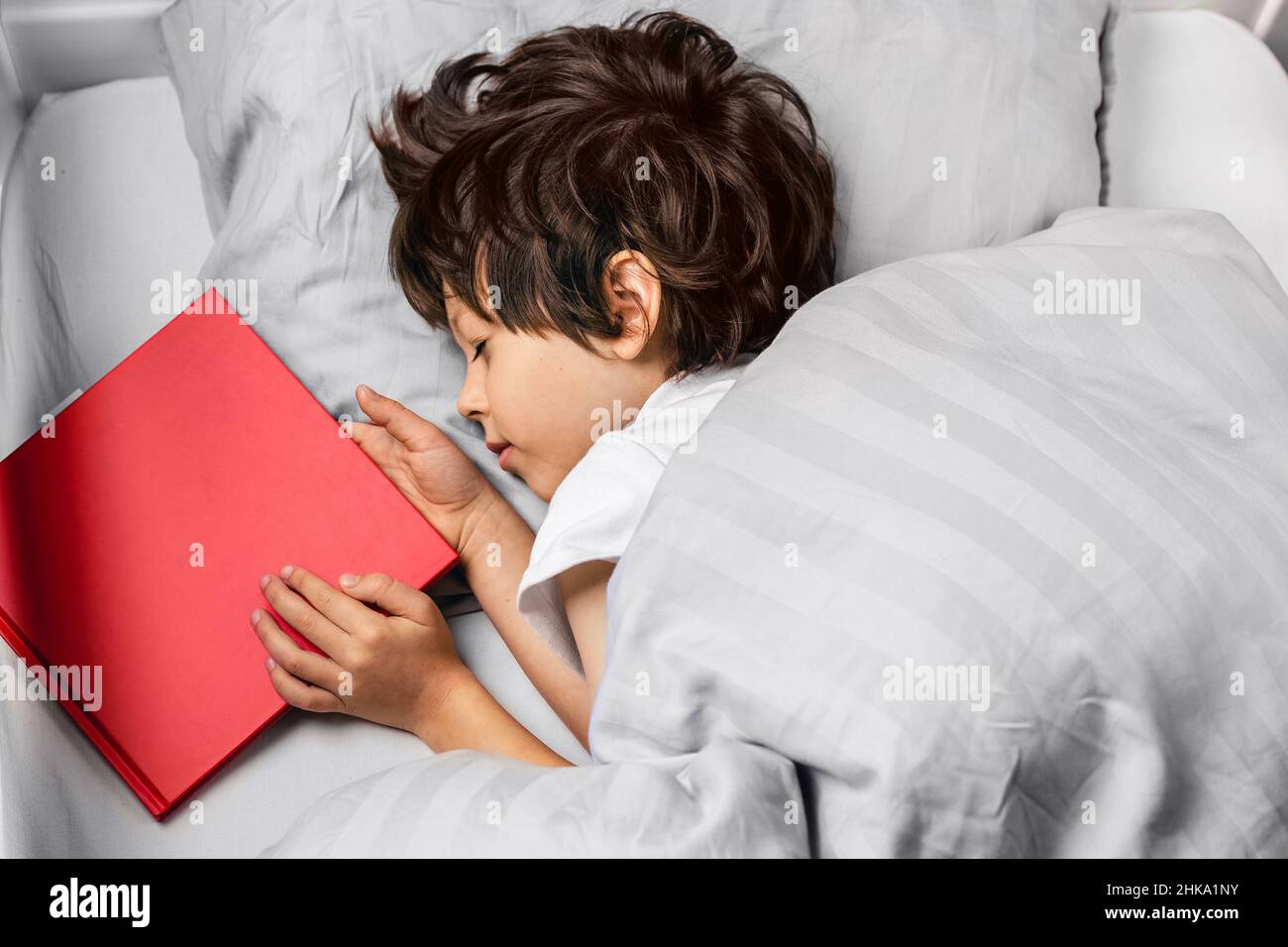 Child sleeping at night in his bed with a red story book. Kids