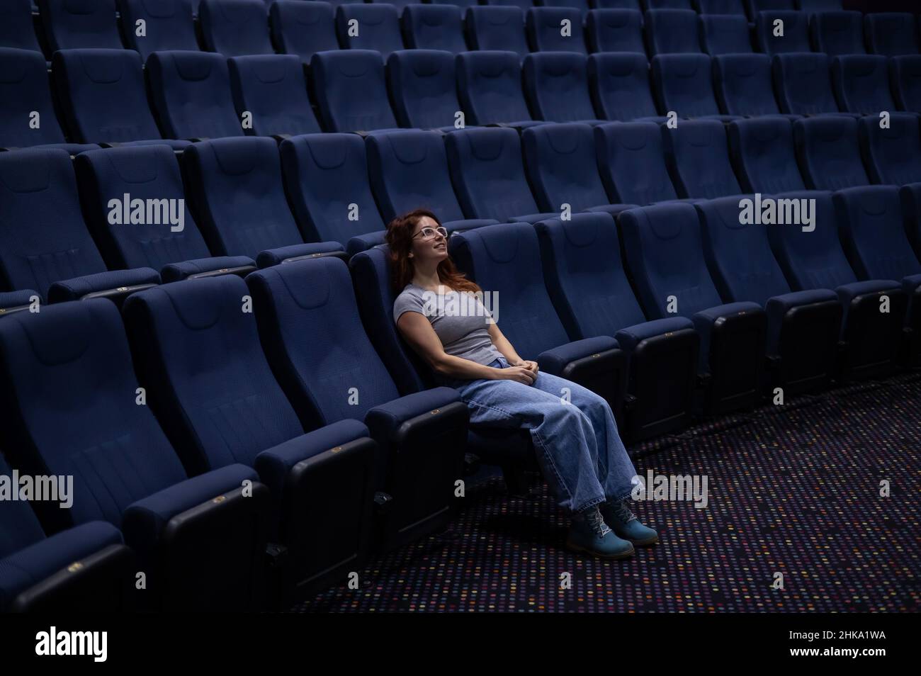 Caucasian redhaired woman sits on the front row in a cinema in an empty hall. The girl is