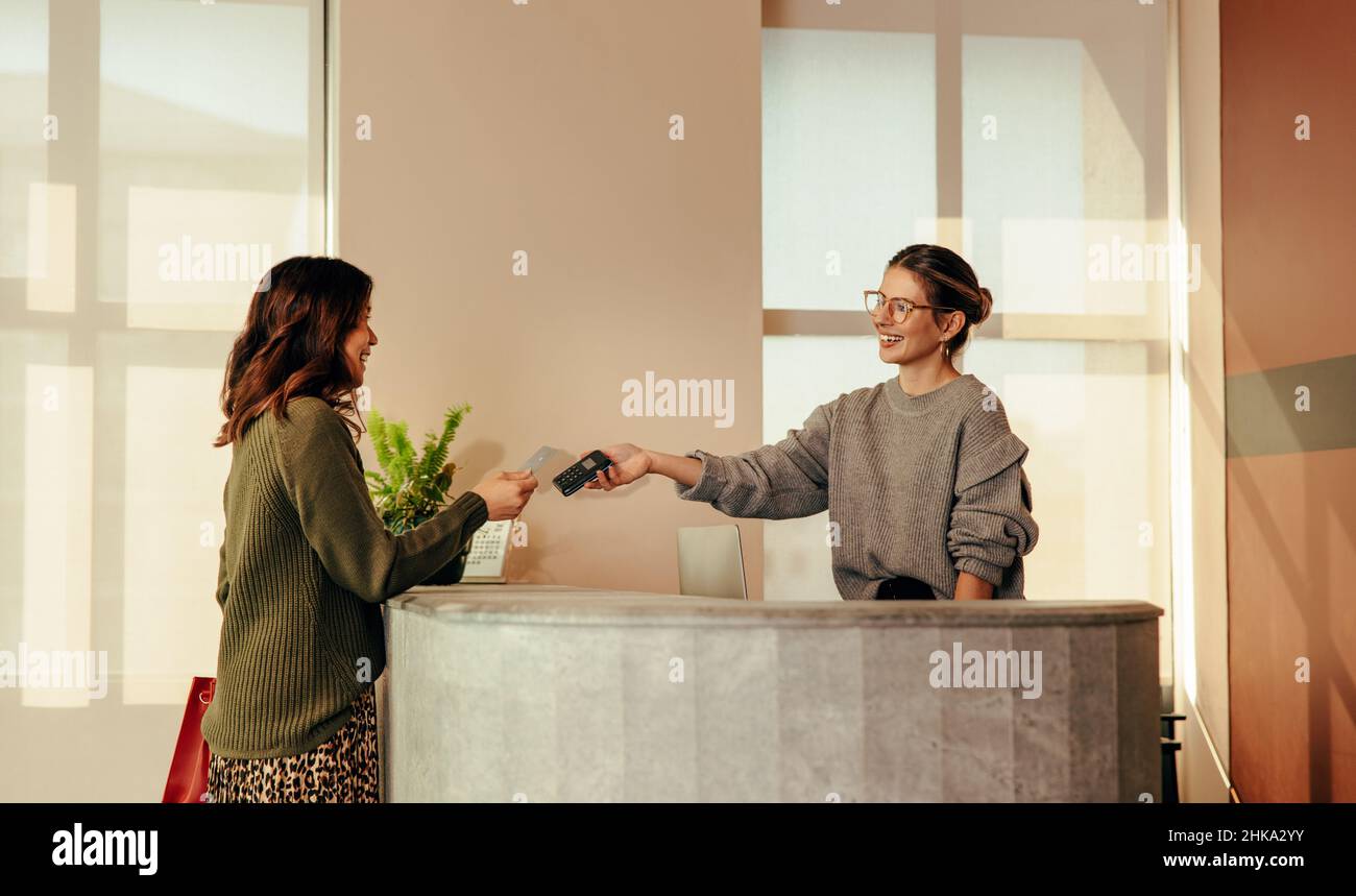 Clothing store assistant taking a credit card payment from a female customer. Happy small business owner smiling cheerfully while assisting her custom Stock Photo