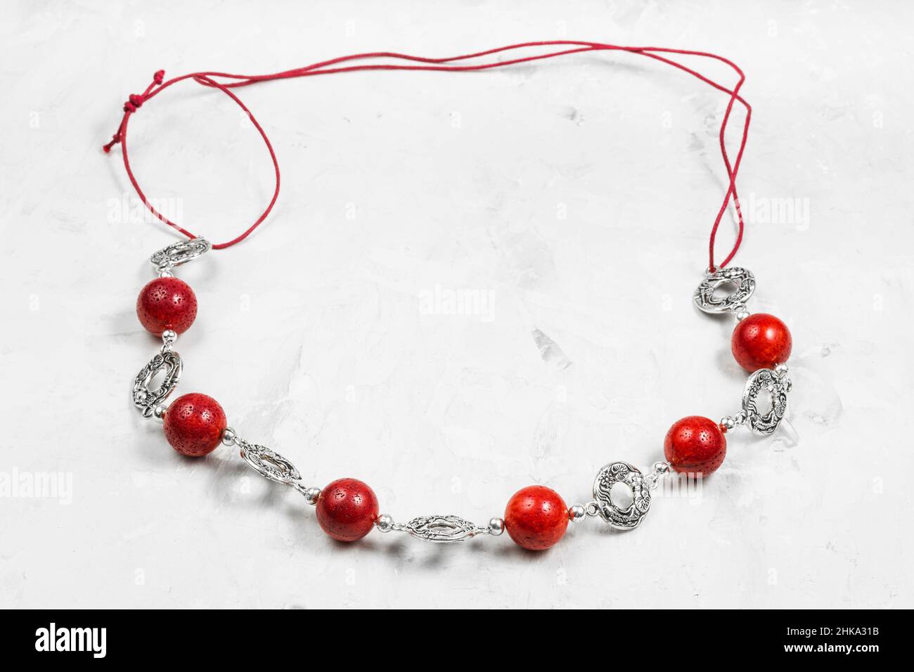 handcrafted necklace of polished red coral balls and decorated silver rings on red leather cord close up on gray concrete board Stock Photo