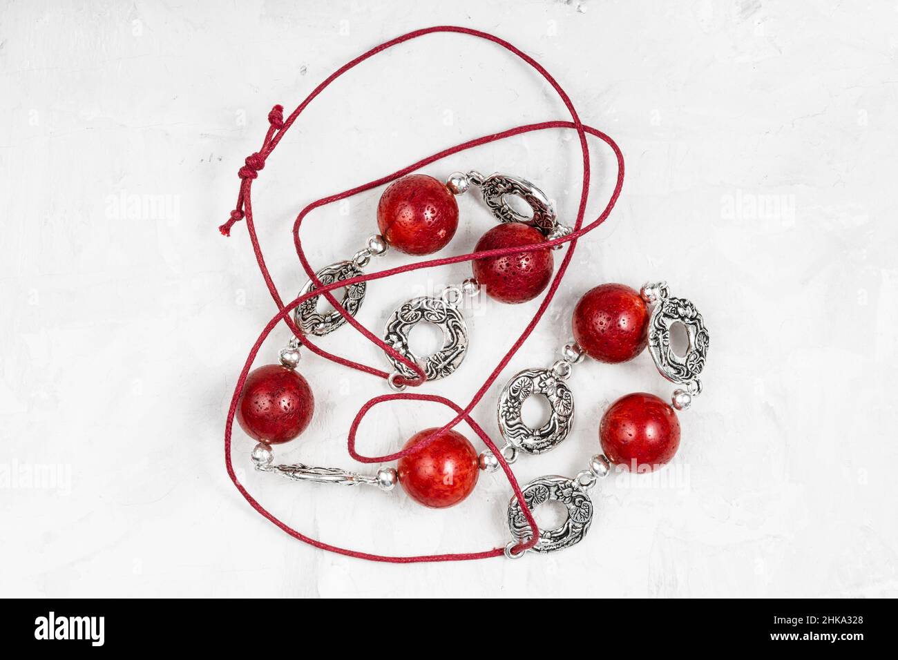 tangled handcrafted necklace of polished red coral balls and decorated silver rings on red leather cord on gray concrete board Stock Photo