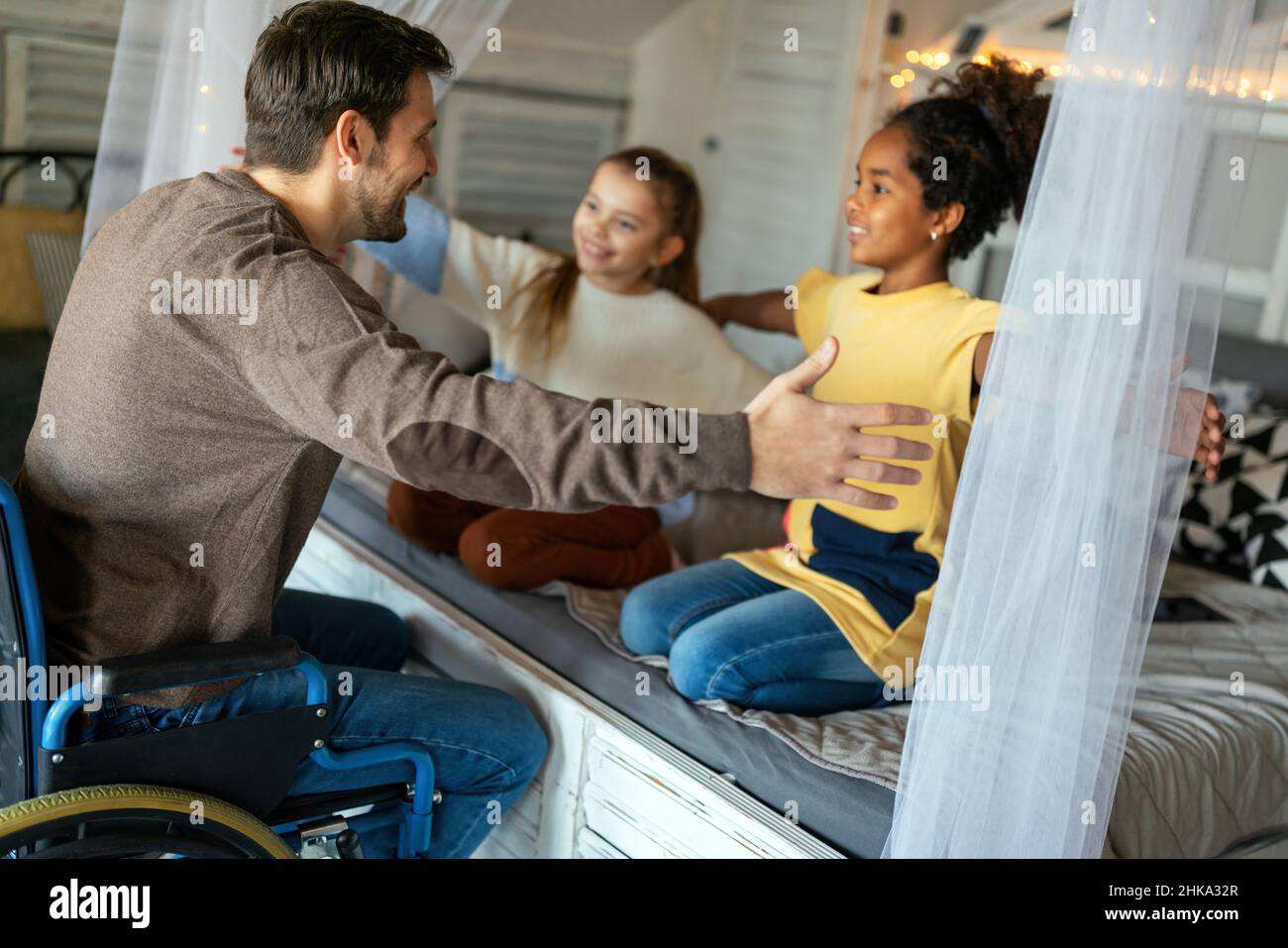 Happy family. Smiling father with disability in wheelchair hugging with children at home Stock Photo