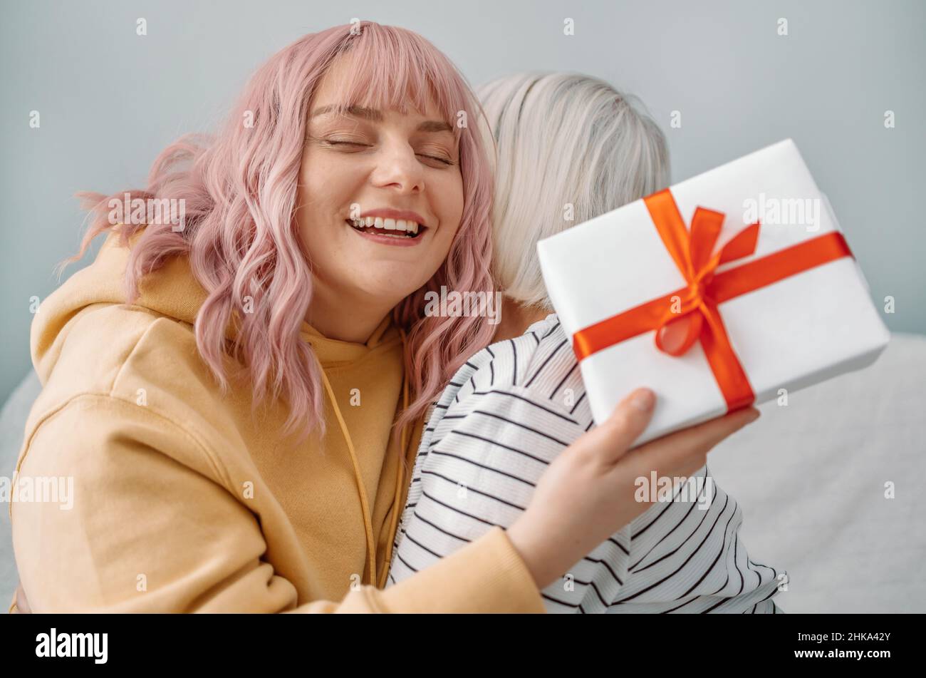Happy Caucasian woman gets gift from daughter at home. Celebrating International Women Day, 8 march, mothers day, birthday Stock Photo