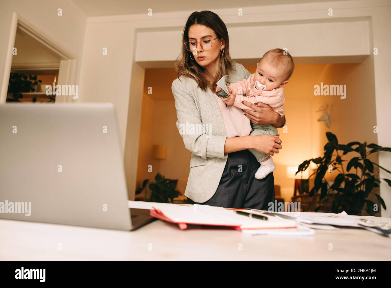 Professional interior designer holding her baby while working in her home office. Multitasking mom planning a new creative project at her desk. Busine Stock Photo