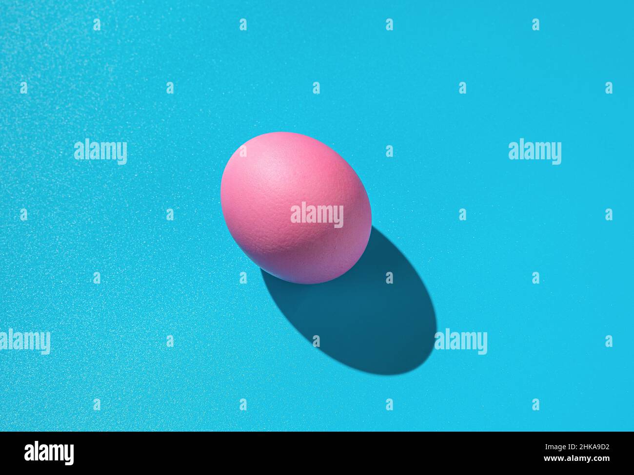 Pink egg on a blue background with a hard shadow. Abstract Easter background. Stock Photo