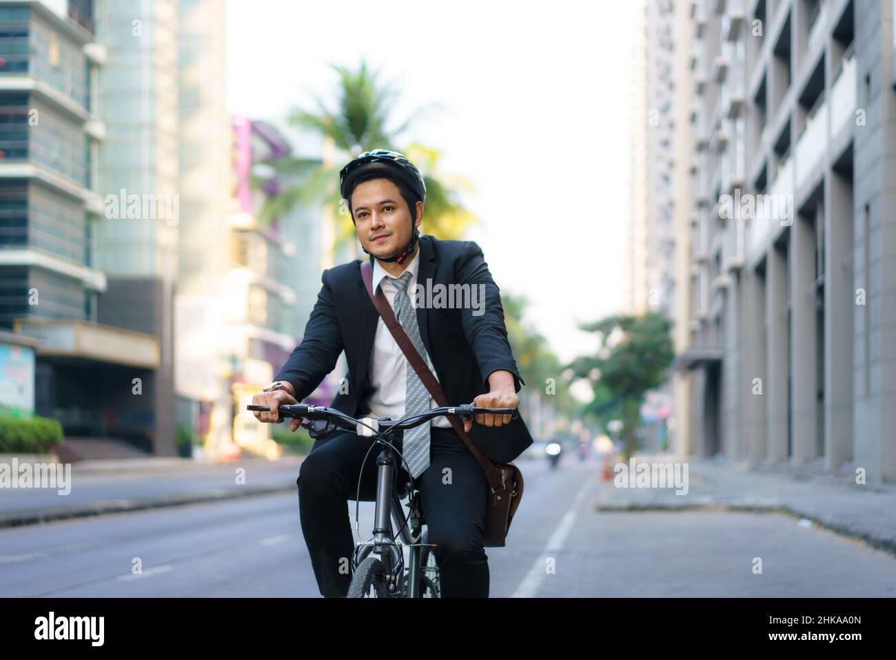 Asian businessman in a suit is riding a bicycle on the city streets for his morning commute to work. Eco Transportation Concept. Stock Photo