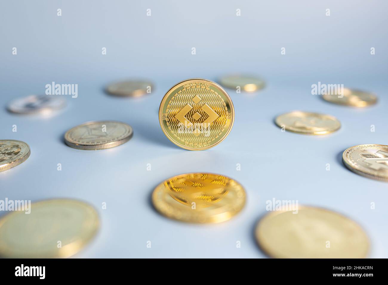 Binance coin standing centrally placed among bunch of cryptocurrency coins on blue background. Banner with golden BNB crypto token. Close-up, soft focus. Stock Photo