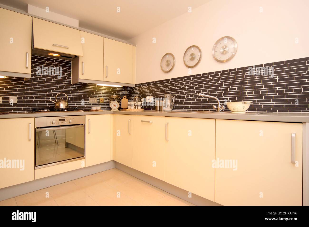 Pale yellow modern kitchen, tiled floor and walls, cooker hood, modern scheme. Stock Photo