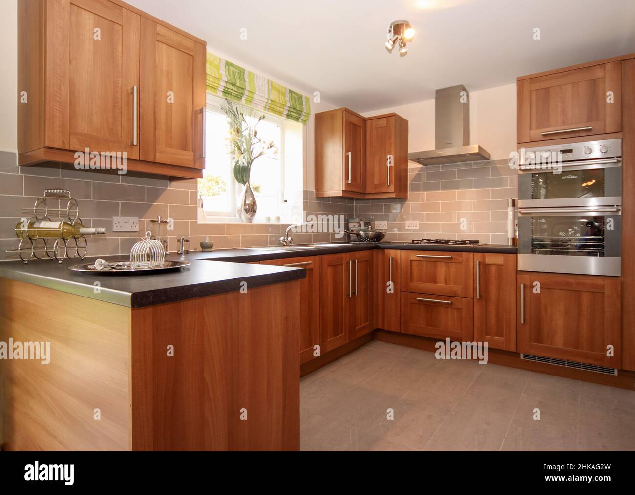 Kitchen with wood finish cabinets fittings, stainless steel double oven, tiled floor, cooker hood. Stock Photo
