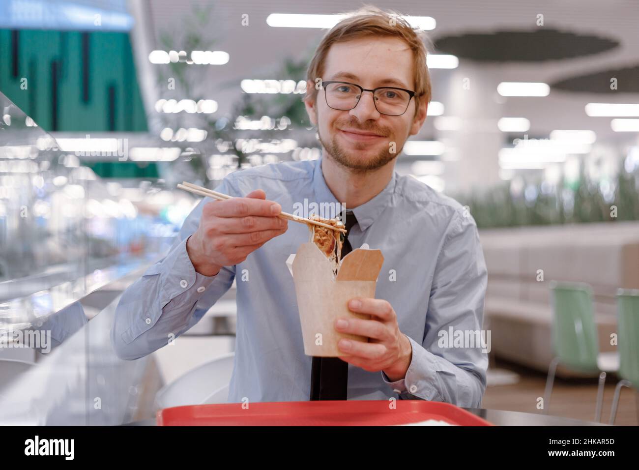 Portrait of smiling businessman with chopsticks eating chinese wok from box on food court. Lunch time. Stock Photo