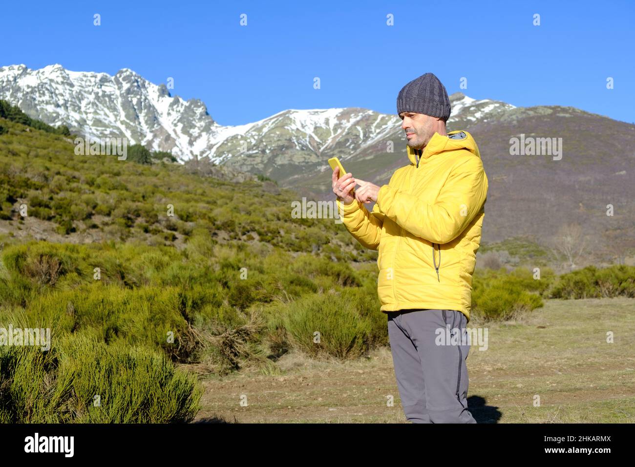a man uses his smartphone in the wilderness near snow-capped mountains Stock Photo